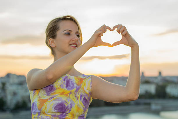 istock Sunset sky with woman hands making heart shape 592361318