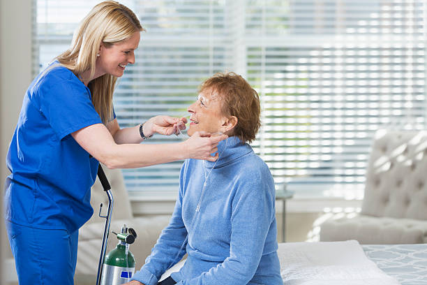 Home healthcare nurse helping elderly woman with oxygen Home healthcare worker helping a senior woman with her oxygen tank. They are in the woman's bedroom. The nurse is wearing blue scrubs. They are smiling and looking at each other. medical oxygen equipment stock pictures, royalty-free photos & images