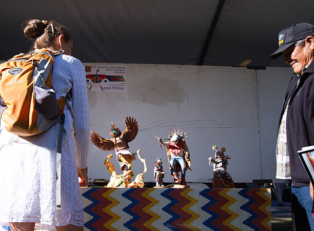 2016 Santa Fe Indian Market: Hopi Sculptor with Kachina Dolls Santa Fe, NM, USA - August 21, 2016: Hopi artist Loren Phillips with his Kachina doll carvings at the 2016 Santa Fe Indian Market. The market, now in its 95th year, is spread out all around the historic Santa Fe Plaza, showcasing North American Indigenous arts and culture. About 1,000 artists from 220 tribes participate in the two-day event; visitors number about 175,000. kachina doll stock pictures, royalty-free photos & images