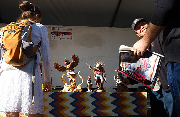 2016 Santa Fe Indian Market: Hopi Sculptor with Kachina Dolls Santa Fe, NM, USA - August 21, 2016: Hopi artist Loren Phillips with his Kachina doll carvings at the 2016 Santa Fe Indian Market. The market, now in its 95th year, is spread out all around the historic Santa Fe Plaza, showcasing North American Indigenous arts and culture. About 1,000 artists from 220 tribes participate in the two-day event; visitors number about 175,000. kachina doll stock pictures, royalty-free photos & images