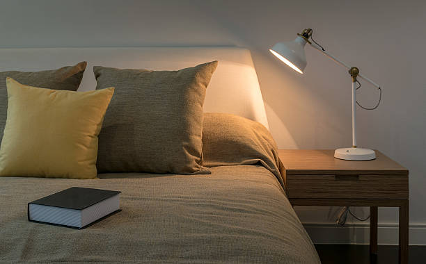 gemütliches schlafzimmer-interieur mit buch und leselampe auf dem tisch - cushion light bed bedroom stock-fotos und bilder