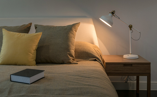 Acogedor interior del dormitorio con libro y lámpara de lectura sobre mesa photo