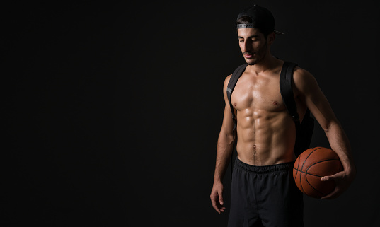 Muscular basketball player in black background indoors horizontal shot.