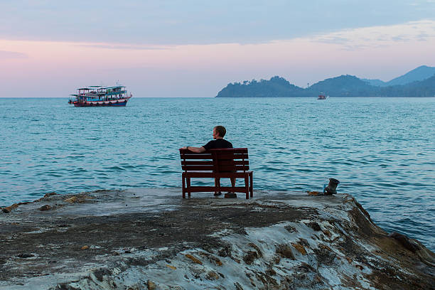 istock Young man sits lonely at the seaside at dusk. 592383946