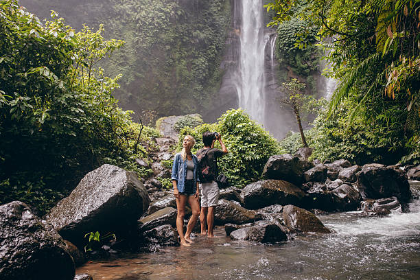 istock Young couple standing by the stream near the waterfall 592384782