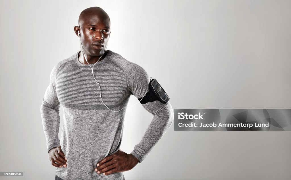 Handsome young african man looking at copy space Shot of handsome young african man in long sleeve shirt listening to music and looking away. Fit male model standing with his hands on hips against grey background Fashion Stock Photo