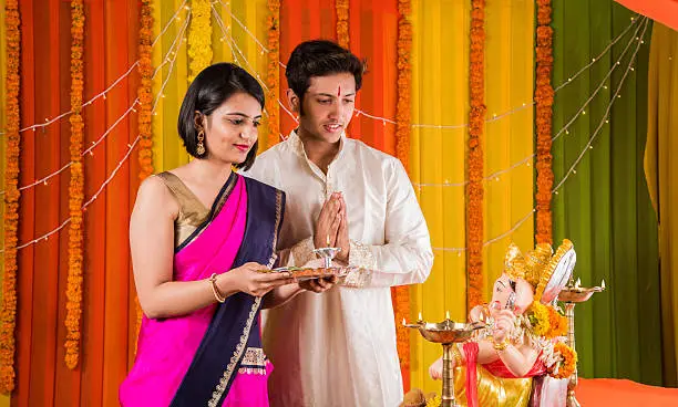 good looking Indian young couple performing puja in front of lord ganesh on ganesh festival or ganesh utsav or ganpati festival