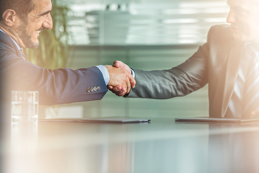 Business manager does handshake with a new employee during a briefing meeting, welcoming her to the team and presenting her to other staff members. Young man shaking hands with trainee. Camera A.