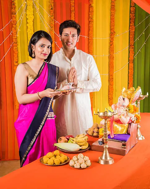 good looking Indian young couple performing puja in front of lord ganesh on ganesh festival or ganesh utsav or ganpati festival