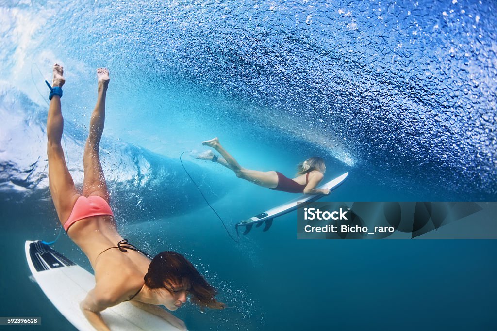 Beautiful surfer girl diving under water with surf board Active girls in bikini in action - surfers with surf board dive underwater under breaking big ocean wave. Family lifestyle, people water sport adventure camp, beach extreme swim on summer vacation Surfing Stock Photo