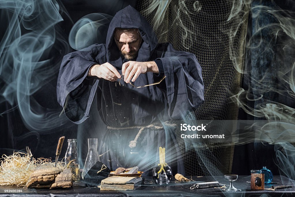 Halloween. The medieval alchemist holds magic ritual smoke Halloween. The medieval alchemist holds magic ritual at the table in his laboratory smoke in the background Alchemist Stock Photo