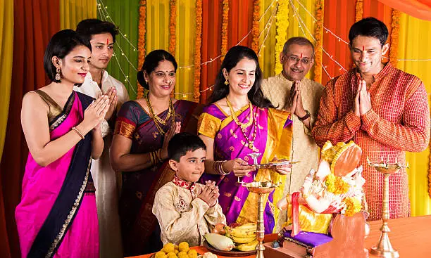 cheerful indian family celebrating or praying Lord Ganesh or ganpati bappa on ganesh festival or ganapati festival or ganesh utsav or ganeshotsav at home with puja thali