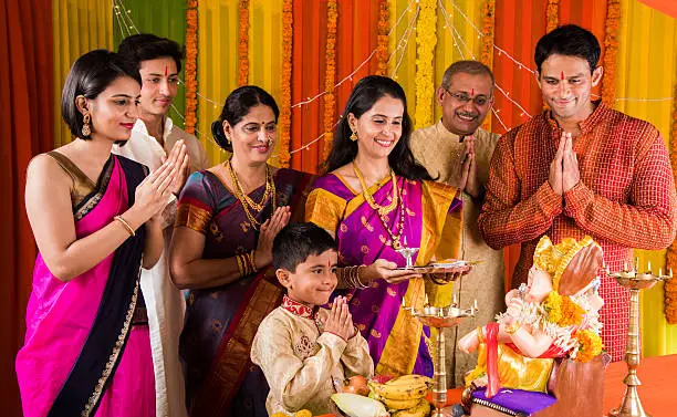 cheerful indian family celebrating or praying Lord Ganesh or ganpati bappa on ganesh festival or ganapati festival or ganesh utsav or ganeshotsav at home with puja thali