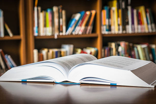 istock Open book on the table in a library and bookshelf 592403590