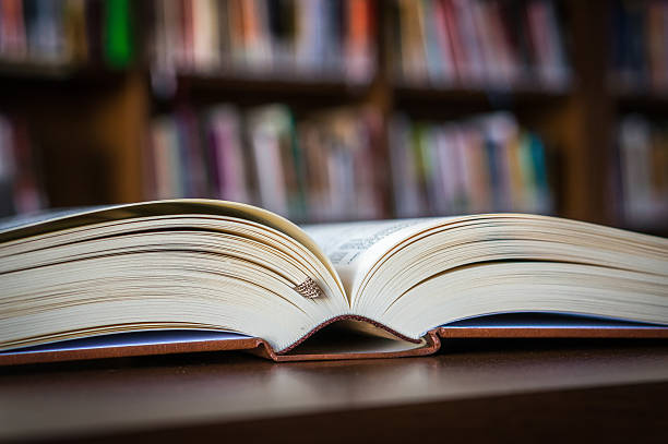 istock Open book on the table in a library and bookshelf 592403612