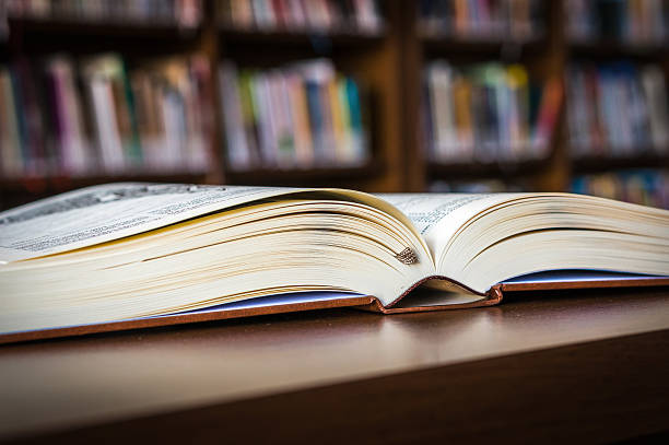 istock Open book on the table in a library and bookshelf 592403648