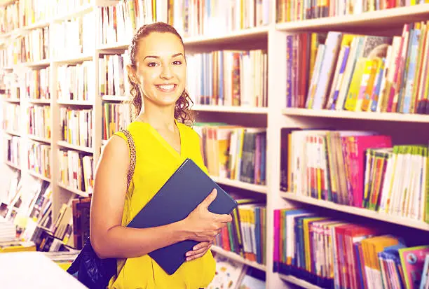 Attractive young woman taking literature books in store with prints