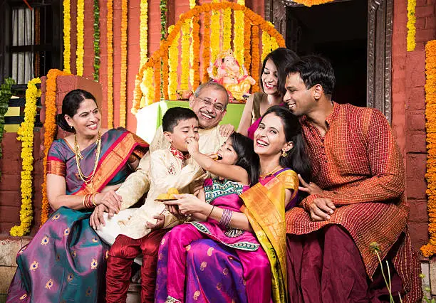 group photo of cheerful indian family eating sweet meets or laddu on  ganesh festival, happy indian family and ganpati festival celebration