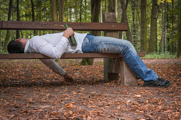 istock Drunk man asleep on a park bench with beer bottles 592408062