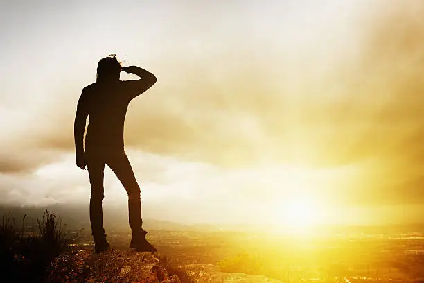 Photo of Young woman seen in silhouette on hilltop watches inspiring sunrise