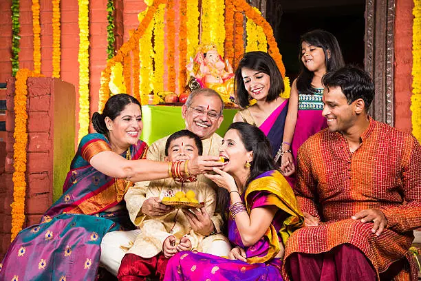 group photo of cheerful indian family eating sweet meets or laddu on  ganesh festival, happy indian family and ganpati festival celebration