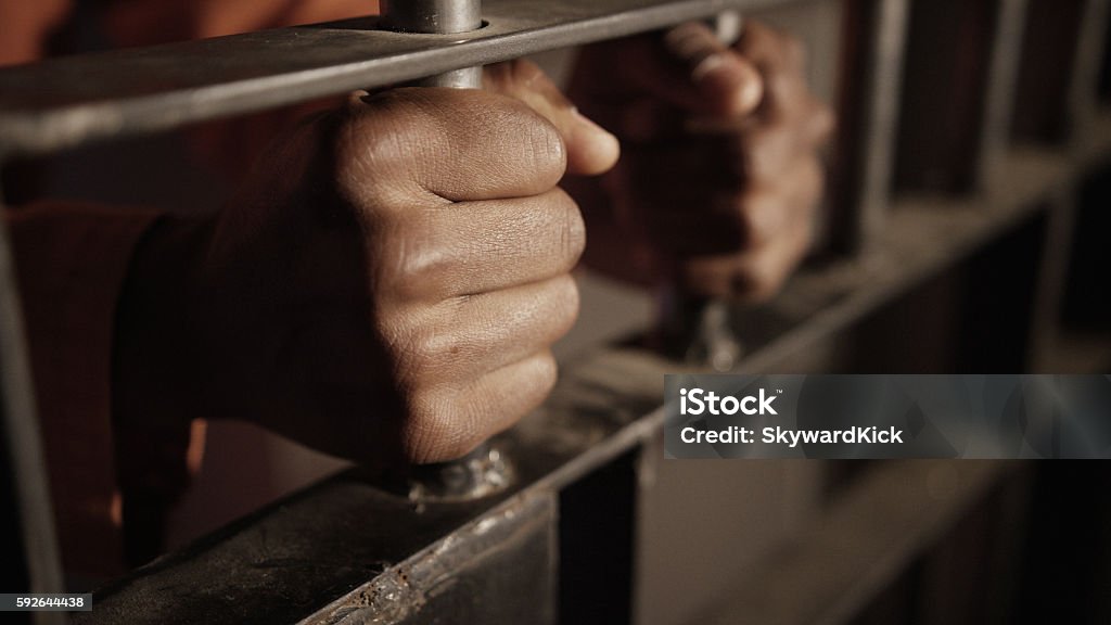 African American Oppression and Prison A man in prison holding the bars of a cell - african american in USA Racial Profiling Stock Photo
