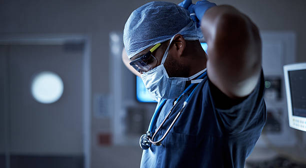Protecting his patient and himself from germs Shot of a surgeon putting on his surgical mask in preparation for a surgery surgeon photos stock pictures, royalty-free photos & images