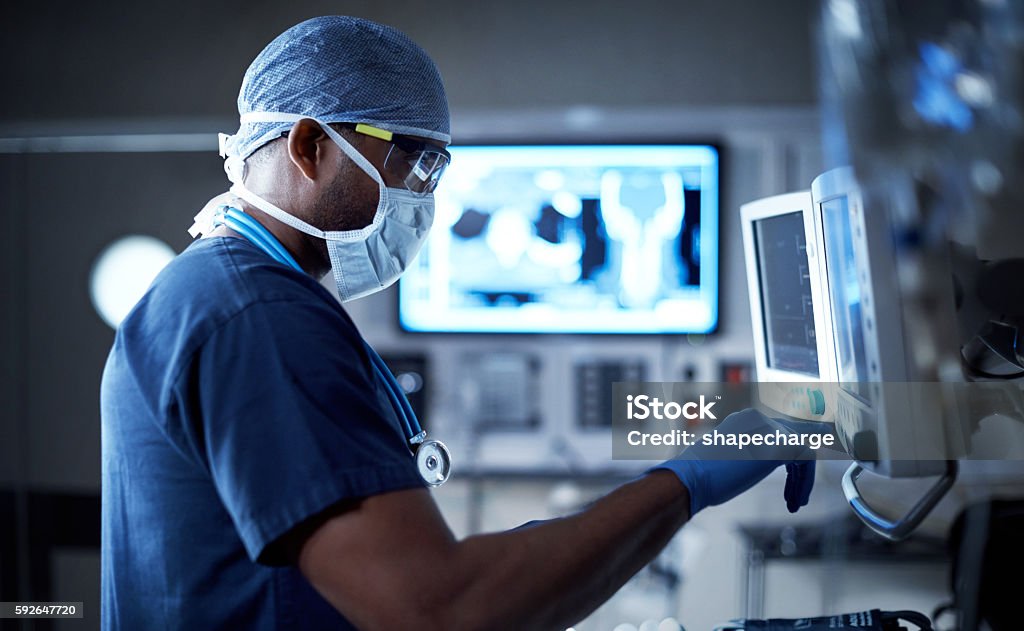Vigilantly monitoring his patient's vitals Shot of a surgeon looking at a monitor in an operating room Healthcare And Medicine Stock Photo