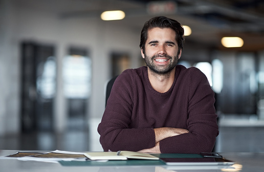 Portrait of a smiling man sitting a desk in a large modern office