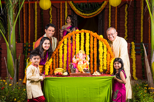 cheerful indian family welcoming lord Ganesha idol on ganesh festival or ganesh chaturthi on palkhi decorated with garland flowers