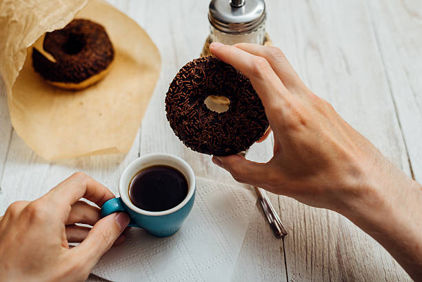 istock Man hands eating chocolate donut with coffee on wooden table 592650640