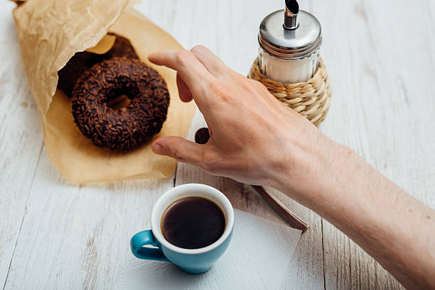 istock Man hands eating chocolate donut with coffee on wooden table 592651074