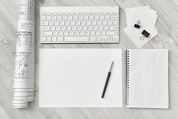 Top view of a draftsman's workplace with a keyboard, a sheet of paper with a pen, a notebook and rolled draft. Creative workspace. Engineering plan. Architecture and draftmanship.