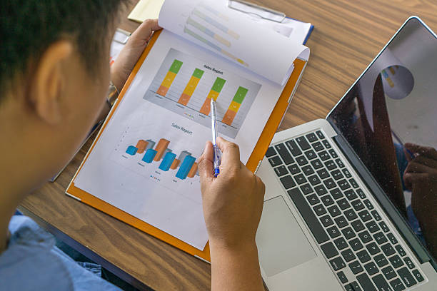istock Close-up of hand holding pen pointing on sales report document 592658792