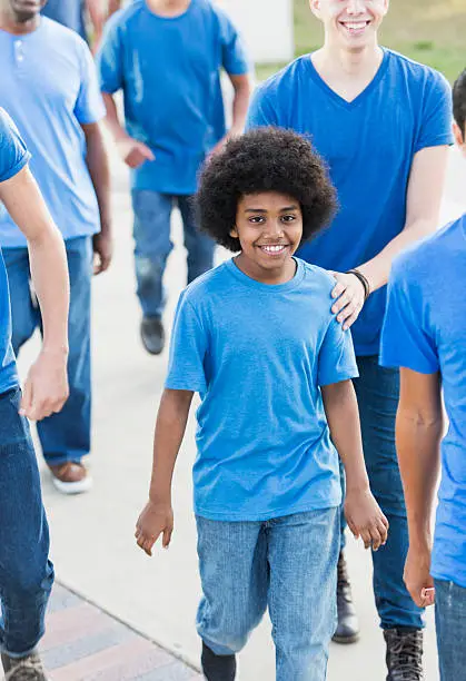Photo of Boy walking with group of men wearing blue shirts
