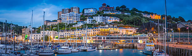 The hotels and villas, quayside shops, pubs and restaurants of Torquay overlooking the harbour illuminated at dusk.