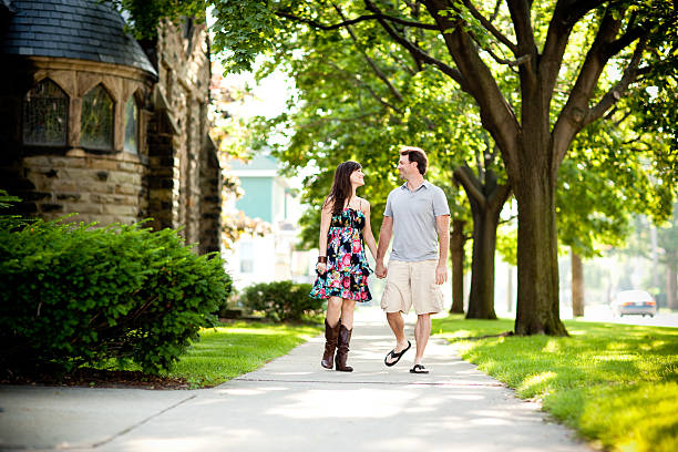 istock Young Man and Woman Holding Hands while Walking on Sidewalk 592666422