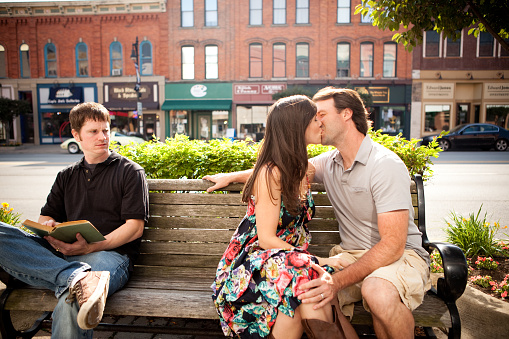 Color stock photo of a young man being irritated with a couple kissing on a bench downtown.