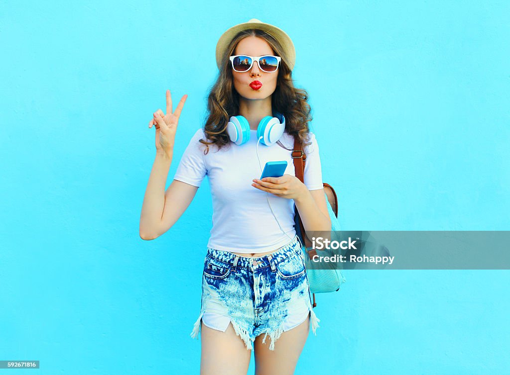 Pretty cool woman listens music and using smartphone over colorf Pretty cool woman listens music and using smartphone over colorful blue background Teenage Girls Stock Photo