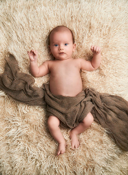 istock Baby boy lying on white sheep fur looking at camera 592672934