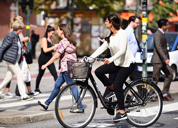 Stockholm, Sweden - August 22, 2016: Summer dressed modern woman bicyclist in profile in environment friendly central Stockholm, Sweden. Panning blur. Traffic, pedestrians and car in background.