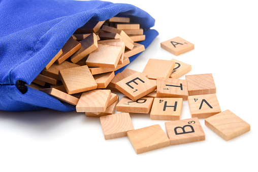 Miami, Florida, USA - December 29, 2015: Lettered wooden tiles mixed up coming out of its bag on white background. Scrabble is a fun and educational game distributed by Hasbro