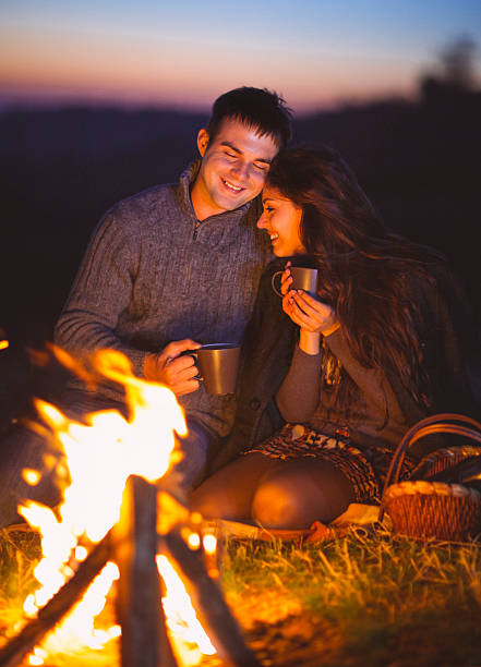 istock Happy couple sitting by fire on autumn beach 592676400