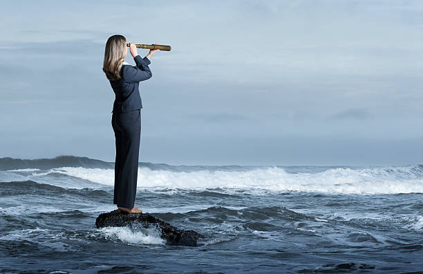 istock Businesswoman Looking Through Spyglass While Standing In Rough Surf 592679082