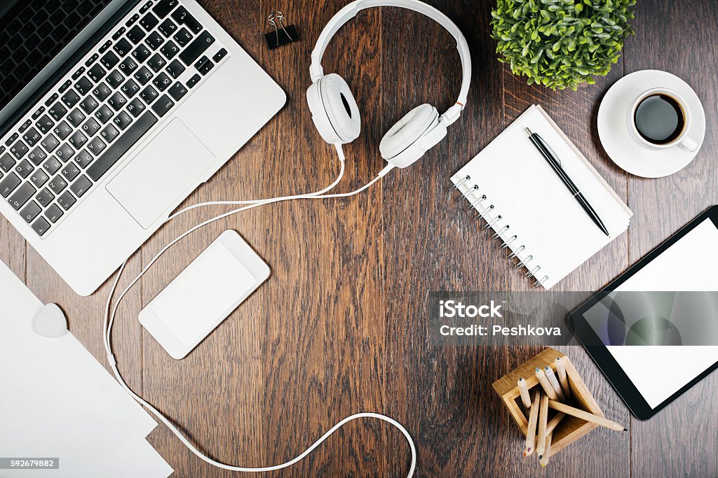 Office desk with technology Top view of wooden desktop with tablet, laptop, white smartphone, headphones, decorative plant and supplies. Mock up Headphones Stock Photo
