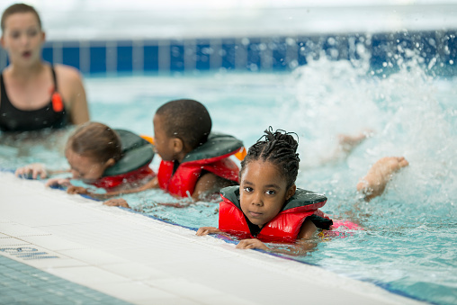 A multi-ethnic group of elementary age children are taking a swim class together at the public pool.