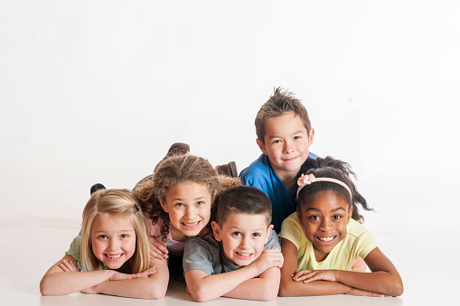 A multi-ethnic group of elementary age children are lying in a group and are smiling while looking at the camera. The background in all white.