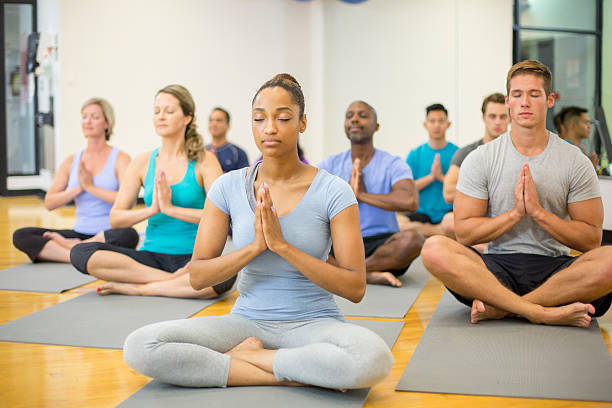 Meditating in Prayer Pose A multi-ethnic group of adults are taking a yoga class at the gym. They are meditating on their yoga mats. yoga class photos stock pictures, royalty-free photos & images