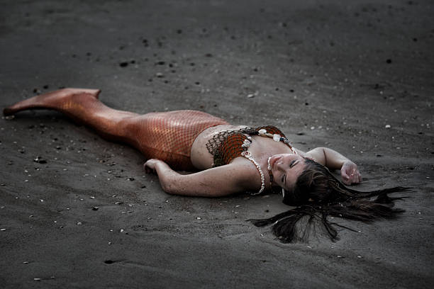 istock Exhausted mermaid lies on sandy beach at night 592687332