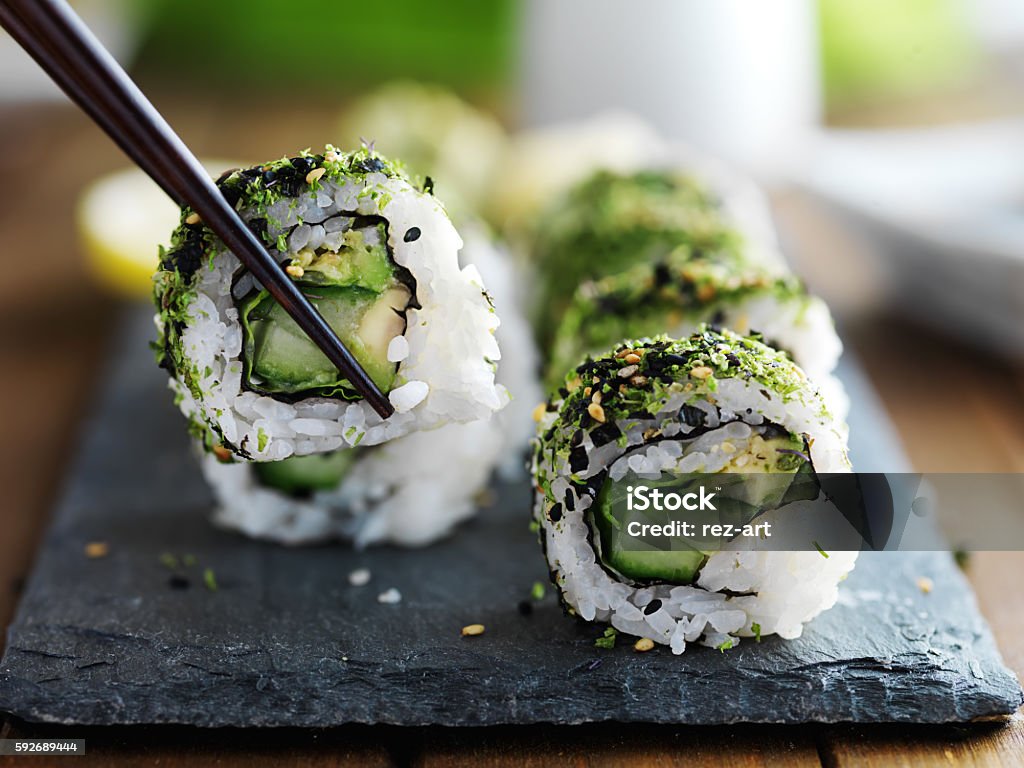 eating healthy kale sushi eating healthy kale and avocado sushi roll with chopsticks Sushi Stock Photo